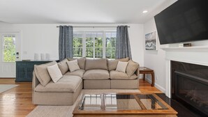 A living room with a sectional sofa, a glass coffee table, a fireplace, and a large TV. - Spacious Pet Friendly-Close to Beach and Town! (Kennebunk)