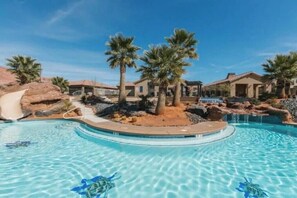 A swimming pool with a slide, palm trees, and houses in the background.