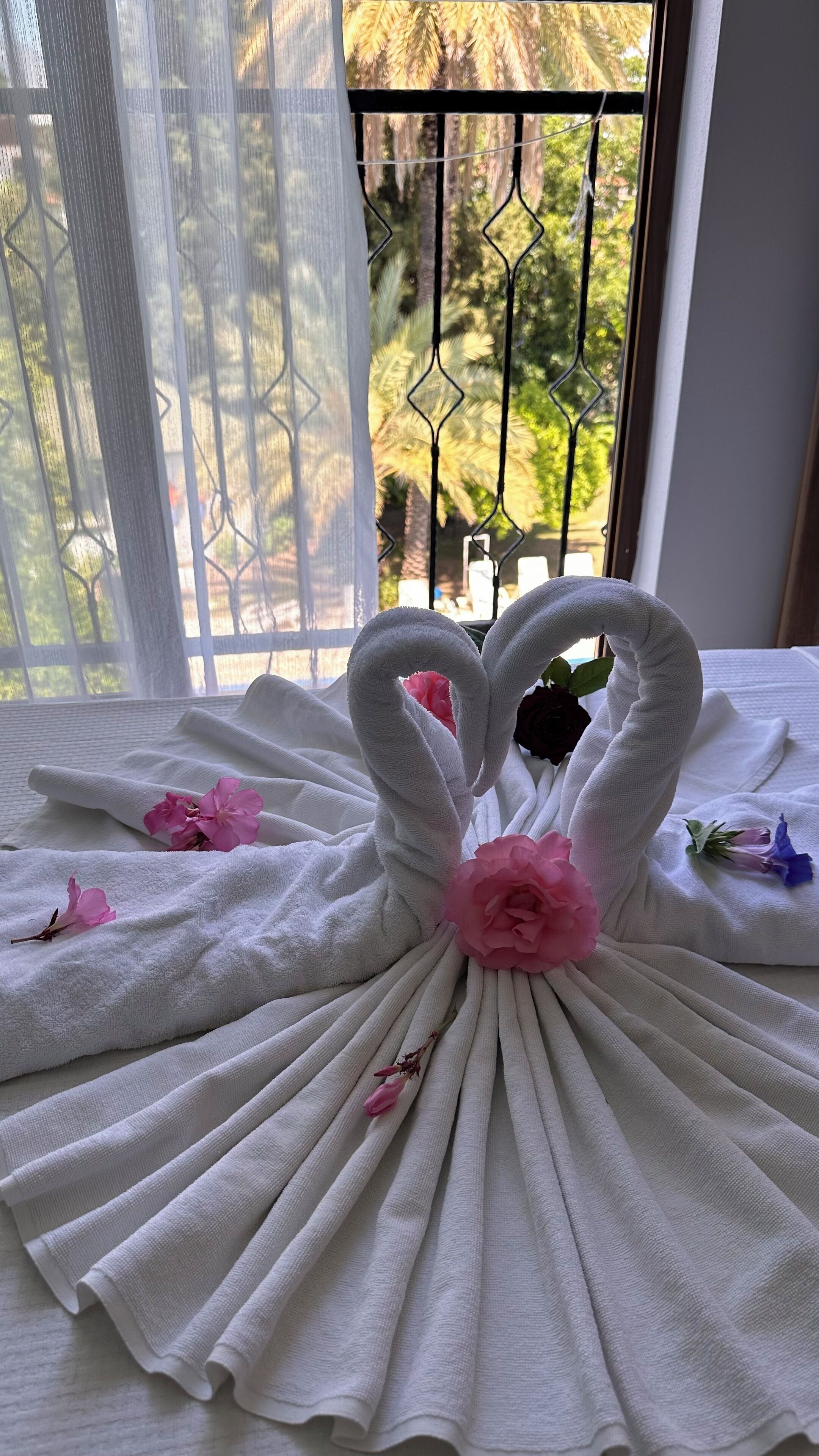 Un lit avec des serviettes blanches disposées en forme de cygne, agrémenté de fleurs roses.