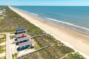 An aerial view of a beachside property with a house, a wooden boardwalk, and a sandy beach. - Beachfront Bliss 4BR House Private Beach Access (Brazoria County)