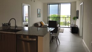 A modern kitchen with a built-in dishwasher, a dining area with a table and chairs, and a balcony with a view of the city. - Modern building, centrally-located condo,2 bedrooms/2 bathrooms, parking space.  (Doral)