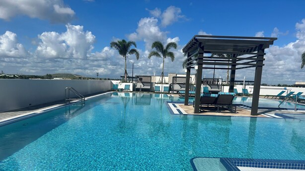 A clear swimming pool with lounge chairs and a pergola, surrounded by palm trees and a clear sky. - Modern building, centrally-located condo,2 bedrooms/2 bathrooms, parking space.  (Doral)