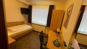 A compact hotel room with a single bed, a small table with a chair, a TV mounted on the wall, and a window with curtains. - Hotel ISHI INN Wolfsburg (Wolfsburg)