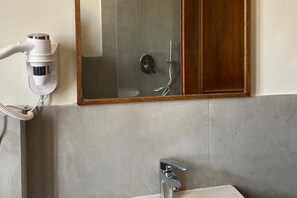 A bathroom with a hairdryer, a mirror, and a shower.