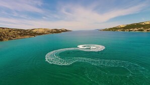 An aerial view of a large body of water with a circular pattern on the surface, surrounded by hills and a distant shoreline with buildings.