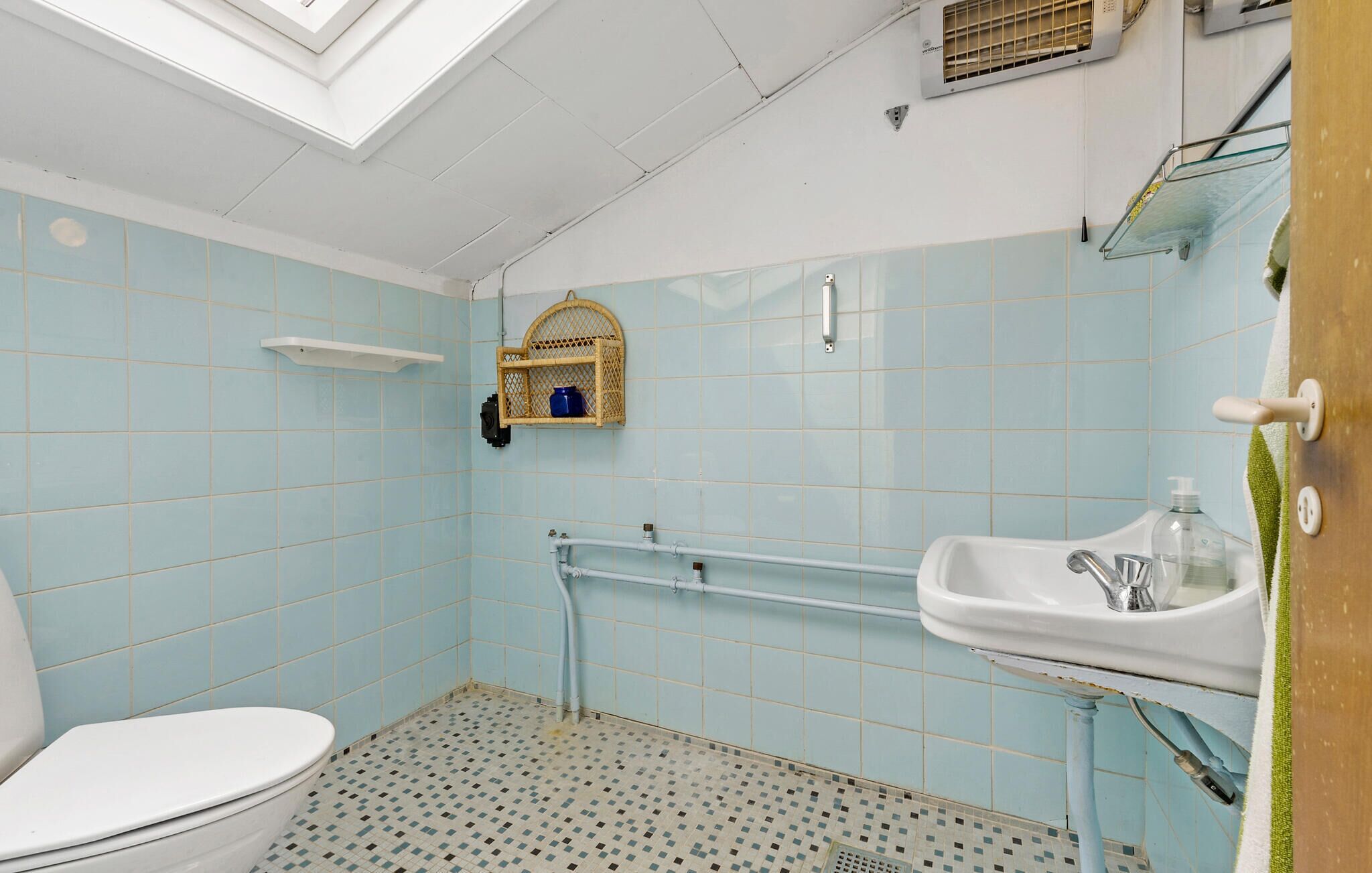 Une salle de bain avec des carreaux bleu clair, des toilettes blanches, un lavabo avec un miroir et un espace douche.