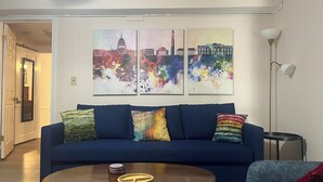 Ett vardagsrum med en blå soffa, ett soffbord och tre färgstarka tavlor på väggen.