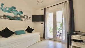 A modern room with a white sofa, a flat-screen TV, a dining table with chairs, and a sliding glass door leading to an outdoor area.