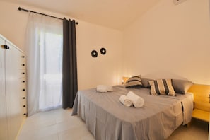 A bedroom with a bed, pillows, a bedside table, a lamp, and a window with curtains.