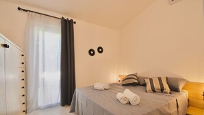 A bedroom with a bed, pillows, a bedside table, a lamp, and a window with curtains.