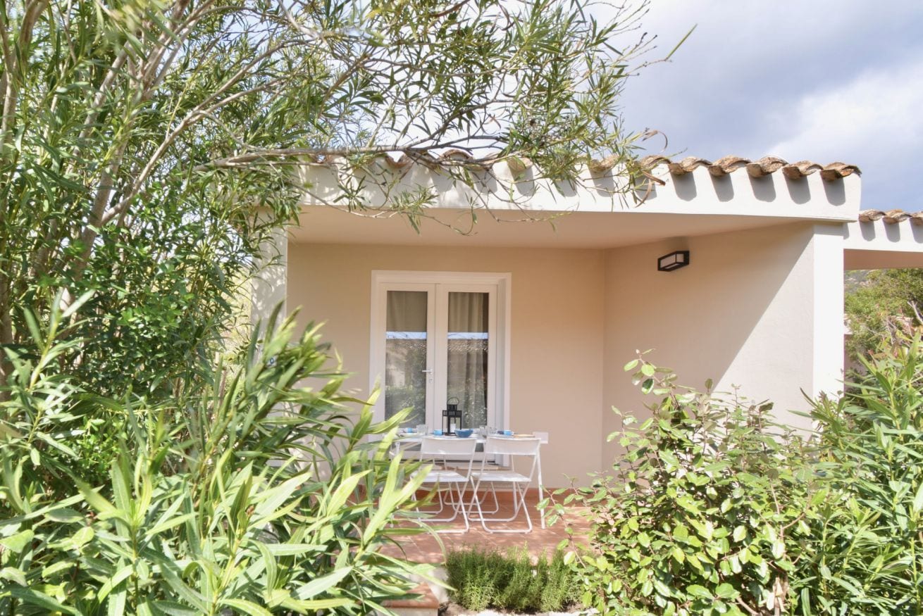 A white building with a tiled roof, a window with curtains, and a table with chairs outside.
