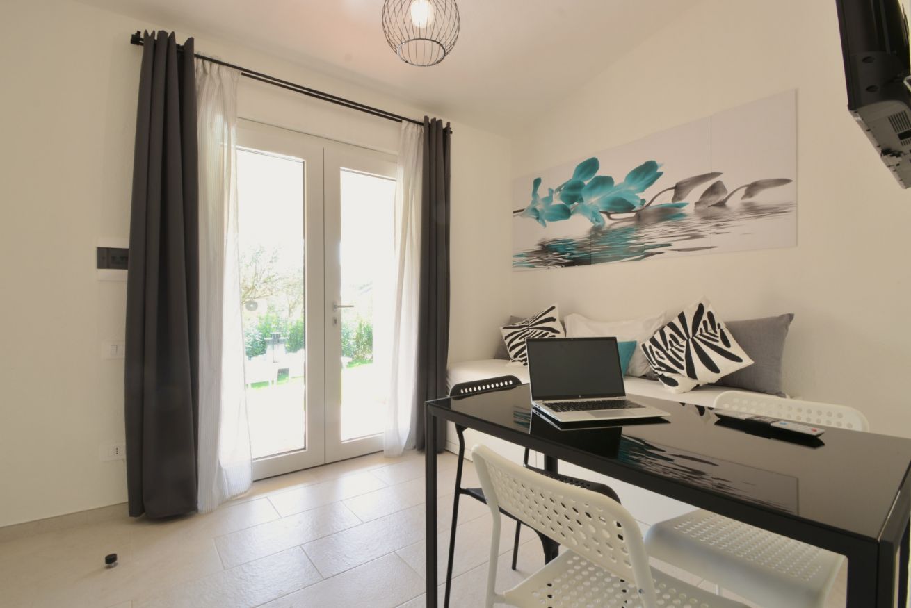 A modern living room with a glass dining table, a laptop, and a sofa with decorative pillows.