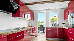 Una cucina moderna con mobili rossi, un piano di lavoro in legno e vista su un patio esterno.