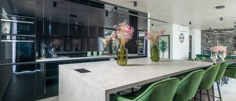 Una cocina moderna con electrodomésticos de acero inoxidable, encimera de mármol y sillas verdes.
