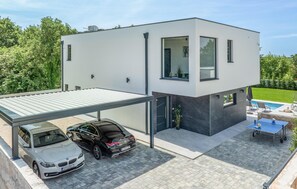 Moderni, kaksikerroksinen talo, jossa on katettu autotalli, uima-allas ja ulkotila oleskelua varten.