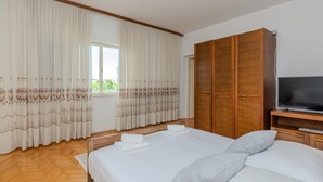 A hotel room with a large bed, a TV, wooden wardrobe, and a window with curtains. - 2 bedroom cozy apartment in Nin (Nin)