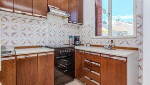A kitchen with wooden cabinets, a black stove, and a window with a view of buildings. - 2 bedroom cozy apartment in Nin (Nin)