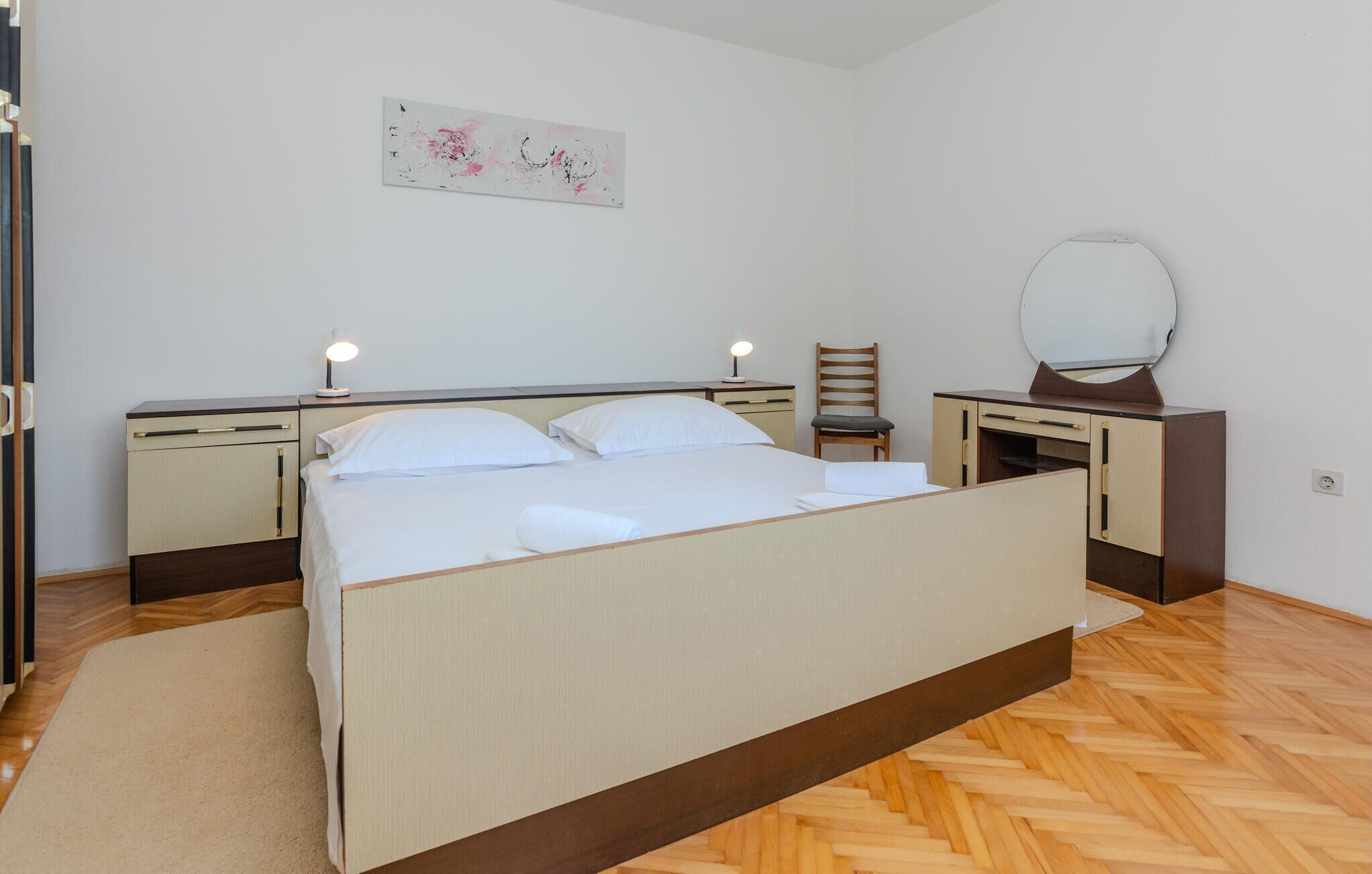 A bedroom with a bed, bedside tables, a chair, a desk, and a mirror.