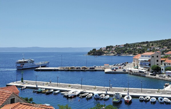 A marina with various boats docked, a large ship in the background, and buildings along the waterfront.
