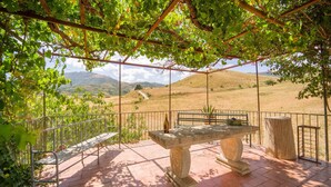 A covered outdoor seating area with a stone table and bench, surrounded by a metal railing, overlooking a hilly landscape. - Awesome home in Palazzo Adriano (Palazzo Adriano)