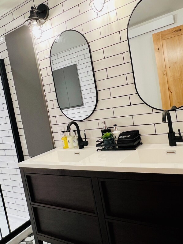 A modern bathroom with a white tiled wall, a large mirror, a black sink, and a wooden cabinet. - Cozy & Modern Retreat. Newly Renovated. Walk to Everything. (Ouray)