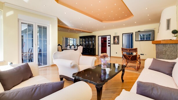A spacious living room with a large sofa set, a coffee table, and a dining area with chairs and a cabinet.