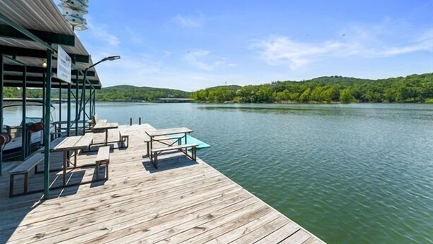 Muelles de madera con mesas y bancos de picnic, con vistas a un lago tranquilo, rodeado de vegetación exuberante.