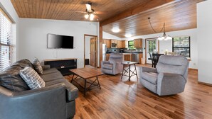 Un salón amplio con techo de madera, un televisor de pantalla plana en la pared, un sofá de cuero y un sillón gris.
