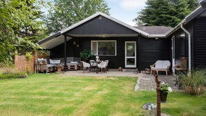 A black wooden house with a covered patio area featuring a sofa set, dining table, and chairs. - 2 bedroom stunning home in Væggerløse (Væggerløse)