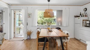 A cozy dining area with a wooden table, wicker pendant light, and a view of greenery outside. - 2 bedroom stunning home in Væggerløse (Væggerløse)