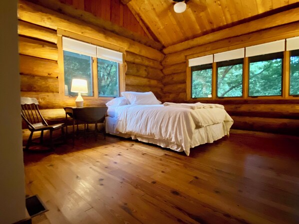 Cozy cabin-style bedroom with a single bed, nightstand, and chair, offering a forest view.