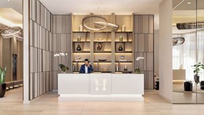 Un área de recepción moderna con un mostrador central, estanterías verticales con adornos y una lámpara de araña grande.