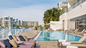 Un área de piscina en la azotea con sillones de descanso, una piscina y vistas de rascacielos.