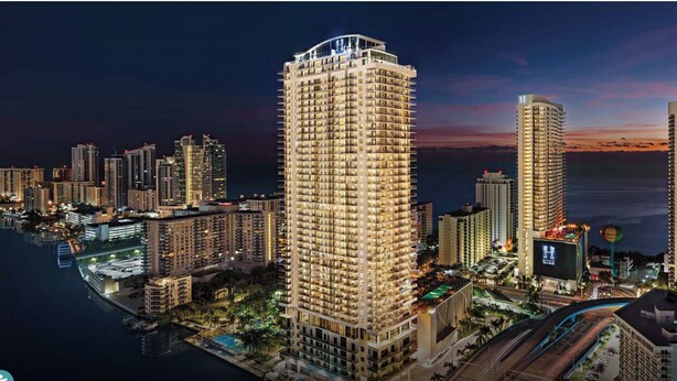 Un hotel moderno de gran altura, con varios pisos, una estructura destacada en la azotea y ubicación frente al mar.