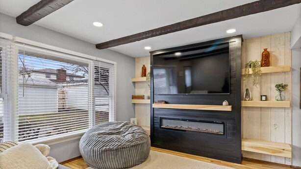 A modern living room with a fireplace, a large flat-screen TV, and wooden shelves. - Spacious 3-BD Townhouse W/PKG 25M From Airport (Milwaukee)