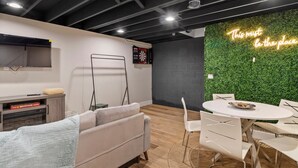 A modern office space with a dartboard, a sofa, a dining table with chairs, and a neon sign on the wall. - Spacious 3-BD Townhouse W/PKG 25M From Airport (Milwaukee)