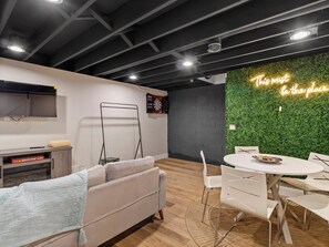 A modern office space with a dartboard, a sofa, a dining table with chairs, and a neon sign on the wall. - Spacious 3-BD Townhouse W/PKG 25M From Airport (Milwaukee)