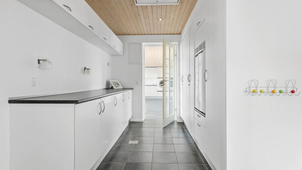 Une cuisine moderne avec des meubles blancs, un plan de travail foncé et un plafond en bois.