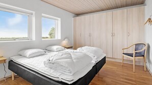 Une chambre à coucher comprenant un lit, deux fenêtres, une armoire, une chaise et une table de chevet avec une lampe.