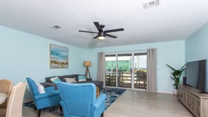 A living room with a blue sofa, two blue armchairs, a coffee table, a TV on a wooden cabinet, and a ceiling fan. - New! Gulf views+Steps to beach+ Arcades+Spacious+Bike (Navarre Beach)