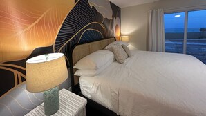 A hotel room with a large bed, a nightstand with a lamp, and a wall mural. - New! Gulf views+Steps to beach+ Arcades+Spacious+Bike (Navarre Beach)