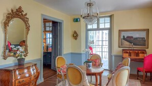 Une pièce comprenant une commode en bois, un grand miroir décoratif, un lustre, une table à manger avec des chaises et un tableau accroché au mur.
