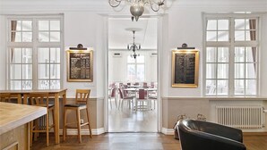 Une salle à manger spacieuse, dotée de hauts plafonds, de lustres et offrant une vue sur une pièce plus petite, accessible par un passage.