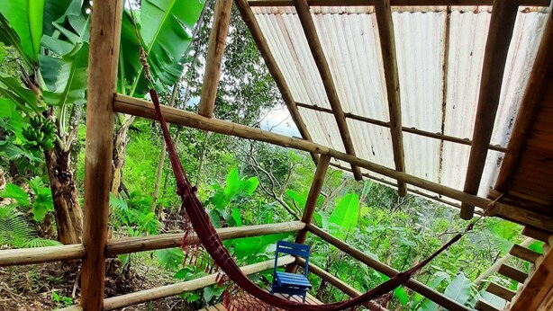 A wooden deck with a hammock and chairs, surrounded by lush greenery. - Chalé Saíra - Eco.hospedagem. Sinta a Natureza Imerso em paz e Tranquilidade (Praia Grande)