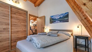 A bedroom with a large bed, wooden ceiling beams, a painting of a mountain landscape, and a desk with a lamp. - Beautiful home in Jasenak with WiFi (Jasenak)