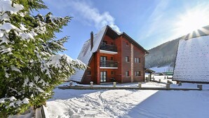 A two-story wooden cabin with a sloped roof, a balcony, and a snow-covered landscape. - Beautiful home in Jasenak with WiFi (Jasenak)