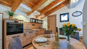 A modern kitchen with wooden beams, a Bosch oven, and a dining area with a round table set for two. - Beautiful home in Jasenak with WiFi (Jasenak)