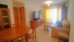 A living room with a sofa, a TV, a dining table with chairs, and a kitchen area with cabinets and a refrigerator.