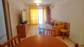 A living room with a wooden dining table, a sofa, and a television on a stand.