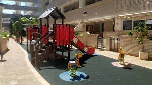 A playground with a slide and climbing structures, surrounded by a brick building with balconies.